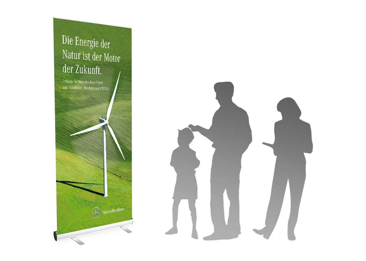 Ein grünes Vollblut-Entega-Banner mit einer Windkraftanlage und deutschem Text steht neben den Silhouetten von zwei Erwachsenen und einem Kind, die die Ausstellung zu beobachten und zu diskutieren scheinen. Am unteren Rand des Banners befindet sich das Mercedes-Benz-Logo.
