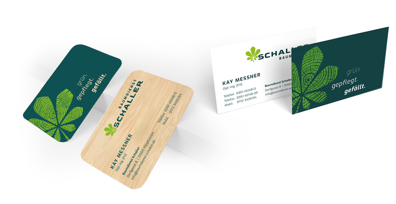 Vier Visitenkarten mit grüner Blattgrafik und dem Text "grün. gepflegt. gefällt.", mit den Kontaktdaten von Kay Meissner und dem Firmenlogo von Schaller Bau, auf weißem und holzstrukturiertem Hintergrund.